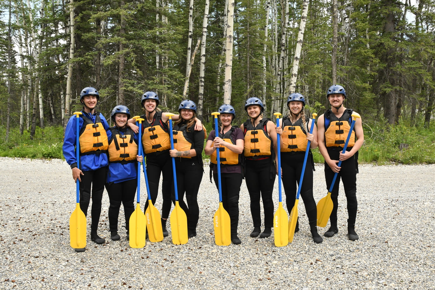Fairshare team on a shore with river rafting gear and paddles.